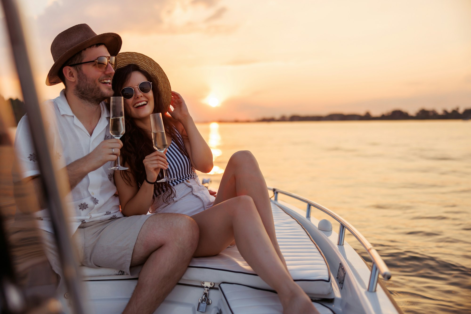 Couple hugging and drinking champagne while sailing to the sunset on a boat. customizable luxury tours in la champagne region of france - Champagne Curated Journeys
